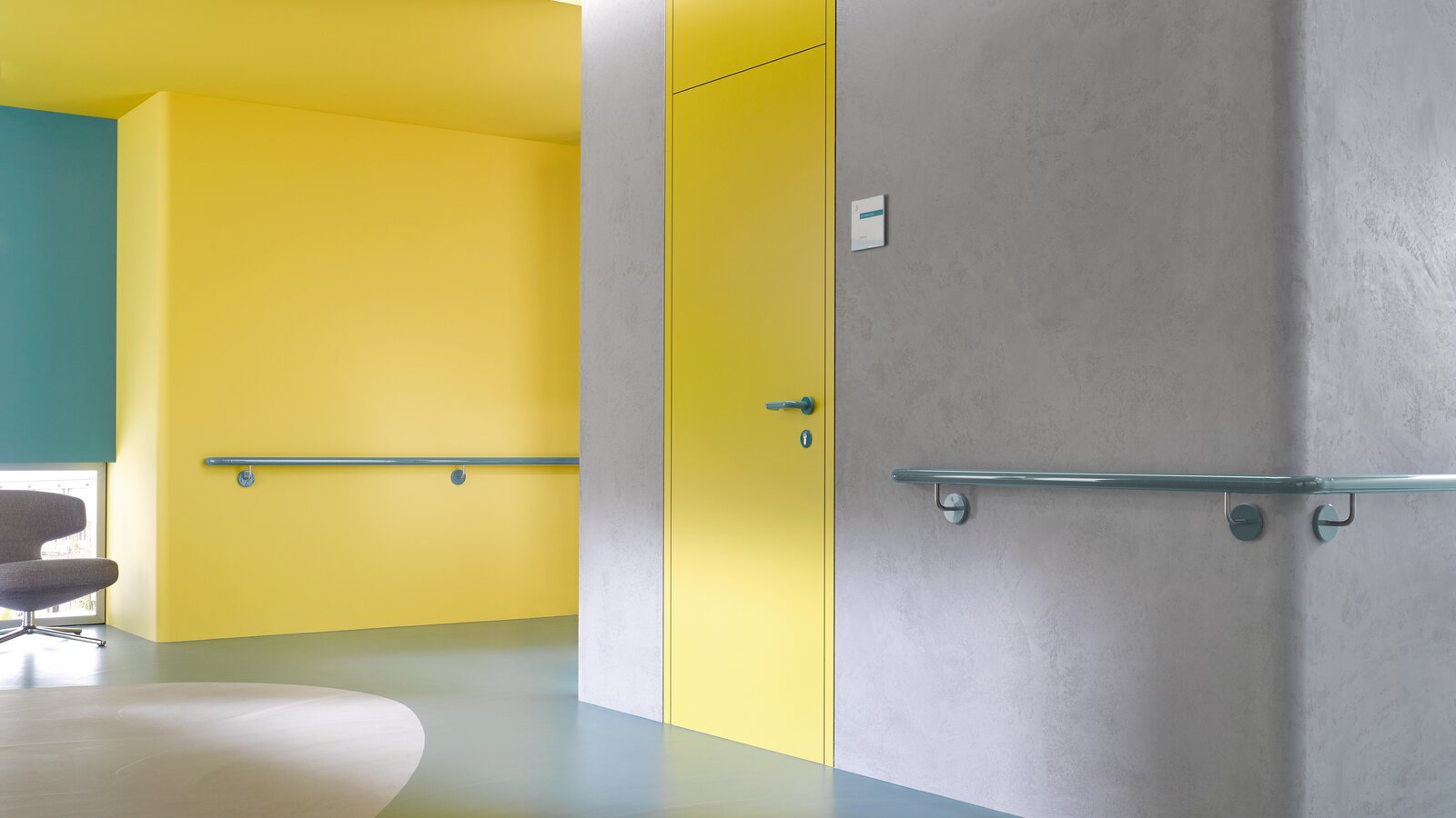 Yellow hallway door equipped with System 111 lever handle in aqua blue and handrail in aqua blue